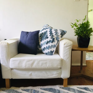 Coastal style denim blue and white square cushion in Aztec pattern styled on a armchair in living room.